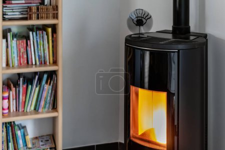Photo for Pellet stove burning with flame in a living room with bookcase and heat diffuser - Royalty Free Image