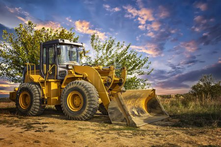 A bulldozer or loader moves the earth at the construction site against the sunset sky