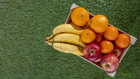 Téléchargez les photos : Caisse de fruits en bois sur herbe avec différents fruits pomme orange banane et mandarine - en image libre de droit