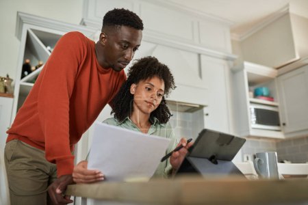Foto de Joven pareja multirracial pagando sus facturas mientras hacen su banca en línea en una tableta digital en casa - Imagen libre de derechos