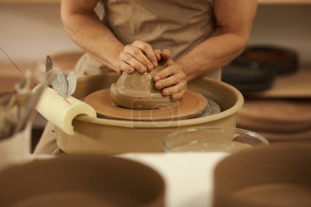 Foto de Primer plano de un alfarero masculino con un delantal formando una pieza húmeda de arcilla en una rueda de cerámica en un estudio de cerámica - Imagen libre de derechos