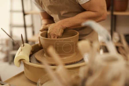 Photo for Close-up of a male ceramist wearing an apron shaping clay on a pottery wheel into a bowl in a ceramics studio - Royalty Free Image