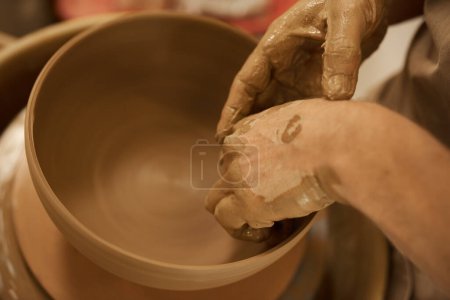 Foto de Primer plano de un alfarero masculino formando un pedazo de arcilla húmeda en un tazón con las manos en una rueda de cerámica en un estudio de cerámica - Imagen libre de derechos
