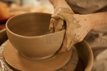 Photo for Close-up of a male potter shaping a piece of clay into a bowl with his wet hands on a pottery wheel in a ceramics studio - Royalty Free Image