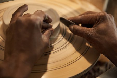 Foto de Primer plano de un fabricante africano de cerámica masculino utilizando una herramienta de mano para dar forma a un tazón girando en una rueda utilizando una herramienta de mano en un estudio de cerámica - Imagen libre de derechos