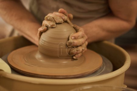 Photo for Close-up of a male ceramist turning a wet piece of clay on a spinning pottery wheel in a ceramics studio - Royalty Free Image