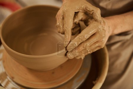 Photo for Close-up of a male potter shaping a piece of wet clay into a bowl on a pottery wheel in a ceramic studio - Royalty Free Image