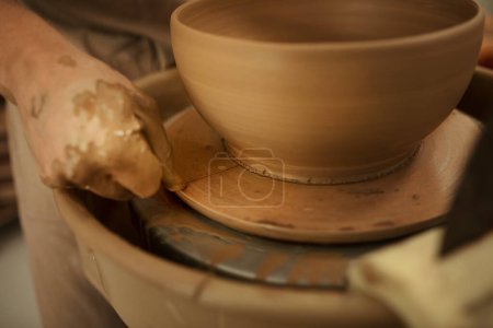 Photo for Close-up of a male potter using a wire to remove a freshly sculpted bowl n a pottery wheel in a ceramic studio - Royalty Free Image