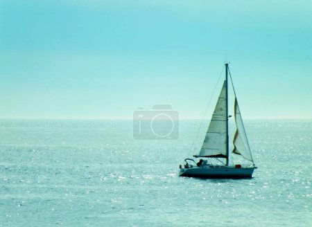 A sailing boat in a beautiful blue sea. Photo of a sailboat in turquoise ocean, sun rays hitting the sea in the afternoon.