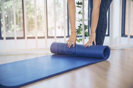 Photo for Woman hands rolled up yoga mat on gym floor in yoga fitness training room. Home workout woman close up hands rolling foam yoga gym mat. Woman barefoot home workout sportive healthy lifestyle concept - Royalty Free Image