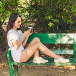 Asian Woman use smartphone drinking coffee hand holding hot disposable cup in green park. Banner Happy Relax asian woman smiling face at outdoors garden. Young women enjoy nature with copy space