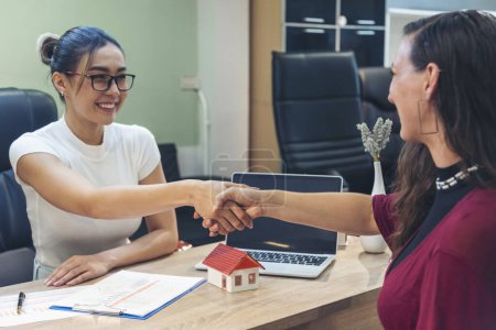Businesswoman shakes hands with customer dealing real estate house agent signing contract. Team diversity women sale house agent office desk. Women handshake sign on insurance mortgage sale document