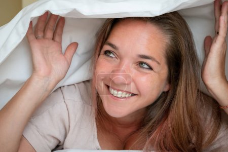 Téléchargez les photos : Jeune femme qui se réveille heureuse. Une femme heureuse sous les draps. Une personne se réveille heureuse d'une sieste - en image libre de droit