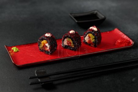 Japanese food: sushi, Roll with cuttlefish ink, mango, salmon, tobiko caviar, avocado. Black background