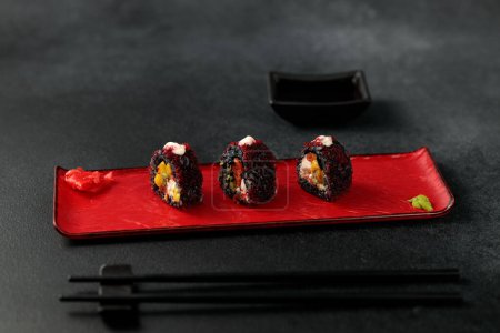 Téléchargez les photos : Japanese food: sushi, Roll with cuttlefish ink, mango, salmon, tobiko caviar, avocado. Black background - en image libre de droit