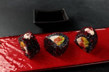 Japanese food: sushi, Roll with cuttlefish ink, mango, salmon, tobiko caviar, avocado. Black background