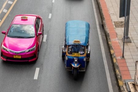 Photo for Tuk tuk driving alongside a pink taxi on a road in Bangkok city center - Royalty Free Image