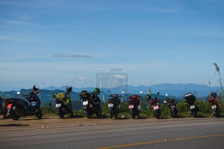 Photo for Pai, Thailand. November 23, 2022. Row of motorbikes parked on the side of the road with beautiful mountain views and blue sky in the background.  Doi Kio Lom viewpoint along the Mae Hong Son Loop. - Royalty Free Image