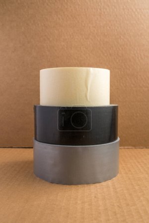 Foto de Tres tipos diferentes de rollos de cinta apilados con el fondo de la caja de cartón marrón - Imagen libre de derechos