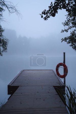 Foto de Muelle de madera en la niebla azul de la mañana, con un anillo salvavidas colgado en un poste - Imagen libre de derechos