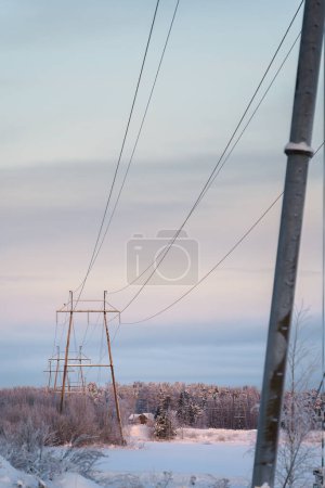 Verschneite Landschaft mit Stromleitungen und Strommasten in der Dämmerung. Lahti, Finnland.