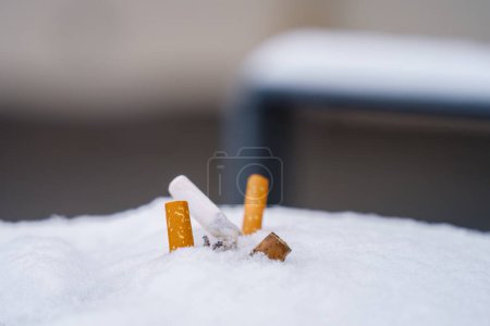 A close-up view of a pile of discarded cigarette butts on snow.