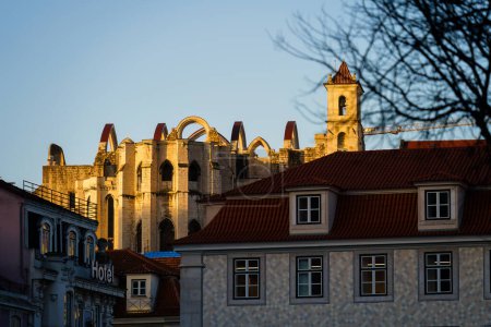 Ruins of Carmo Convent in a golden sunlight behind the historic buildings in Lisbon, Portugal.