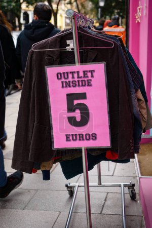 Pinkfarbenes Schild am Kleiderständer außerhalb der Verkaufsstelle innen 5 Euro.