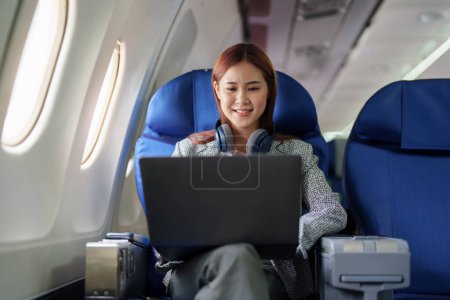 Téléchargez les photos : Portrait d'une femme d'affaires asiatique réussie ou d'une entrepreneure en costume formel dans un avion assis dans un siège de classe affaires et utilise un ordinateur portable pendant le vol. - en image libre de droit