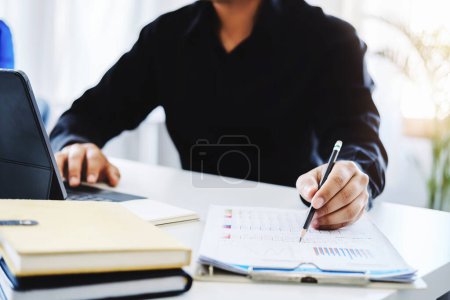 Photo for An accountant, businessman, auditor, economist man holding a pen pointing to a budget document and using tablet to examine and assess financial and investment risks for a company - Royalty Free Image