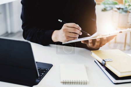 Photo for An accountant, businessman, auditor, economist man holding a pen pointing to a budget document and using tablet to examine and assess financial and investment risks for a company - Royalty Free Image
