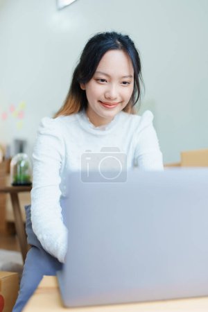 Photo for Starting small business entrepreneur of independent Asian woman smiling using computer laptop with cheerful success of online marketing package box items and SME delivery concept. - Royalty Free Image