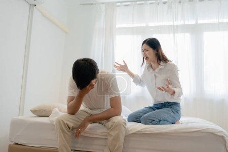 Häusliche Gewalt, asiatische Frau bedroht Ehemann, verängstigter Familienvater umarmt seine Frau, während sie zusammen im Bett sitzt