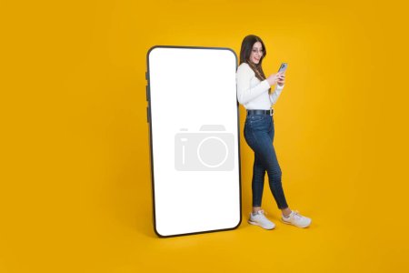 Woman leaning big smartphone, full body view woman leaning big smartphone. Using mobile phone, standing over isolated yellow background. Huge modern phone mockup. Recommending app, website, copy space