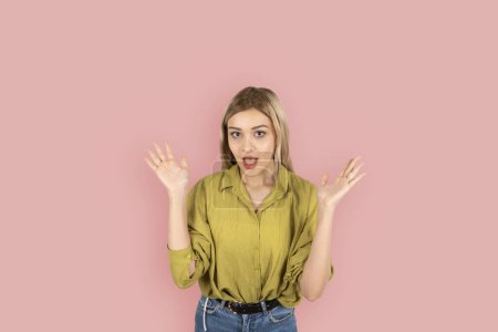 Photo for Surprised woman,  photo of young blonde caucasian surprised woman. Lady 20s wearing green shirt spread hand say awesome, shocked, wow. Isolated pink background studio shot, lifestyle concept. - Royalty Free Image