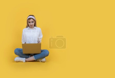 Photo for Unhappy caucasian woman sit floor hold use laptop looking camera angrily. Yellow background, copy space. Having problems, reading negative news. Office worker, female employee having issue with job. - Royalty Free Image