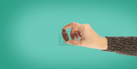 Date fruit, top view image of woman hand holding date fruit with two fingers. Showing, giving, offering special nutrition dessert for breaking fast on Iftar. Ramadan concept image, copy space.