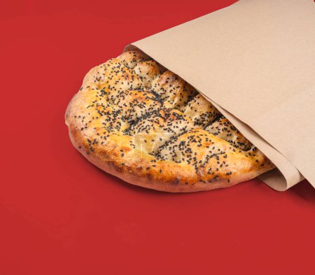 Traditionelles spezielles türkisches Brot namens Ramazan Pide in Papier gewickelt. Isolierter roter Hintergrund, Textbereich kopieren. Heiliger Monat Ramadan pita Konzept Idee Bild.