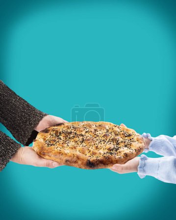 Child and mother holding Turkish cuisine special holy month round Ramadan bread called Ramazan Pide. Turquoise background, copy space. Delicious bakery product with egg, sesame seeds.