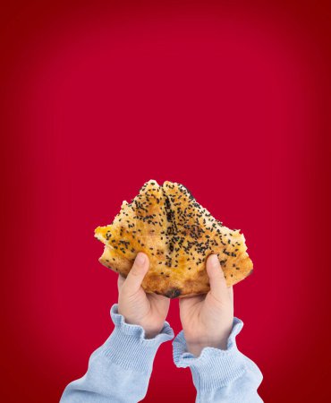 Holding piece of Ramadan pide, top view concept idea image of child hands holding piece of Ramadan pide. Traditional Turkish bread for holy month. Red background, copy space.