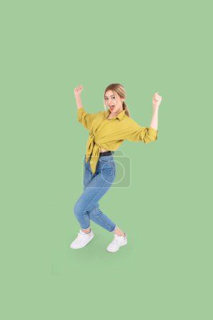 Photo for Full body length excited happy young blonde woman wear yellow shirt and jeans doing winner gesture clenched fists. Isolated green studio background. Copy space. People lifestyle concept. - Royalty Free Image