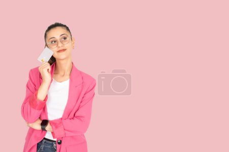 Photo for Dreamful woman, portrait of young caucasian brunette dreamful woman holding credit bank debit card. Looking copy space. Wear formal pink jacket, isolated pastel pink background. Lifestyle concept. - Royalty Free Image