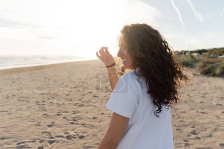 joyeux jeune femme en t-shirt blanc souriant sur la plage de sable en Espagne 