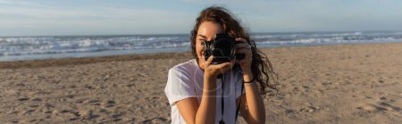 curly woman in white t-shirt taking photo on digital camera in Spain, banner 