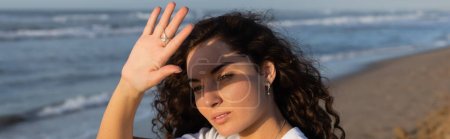 Téléchargez les photos : Portrait of curly woman hiding face from sun on beach near sea, banner - en image libre de droit