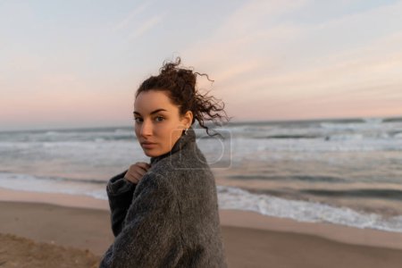 Téléchargez les photos : Portrait de femme bouclée regardant la caméra sur la plage en Espagne - en image libre de droit