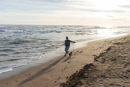 Téléchargez les photos : Jeune femme courant près de chiot chien sur la plage de sable fin à Barcelone - en image libre de droit