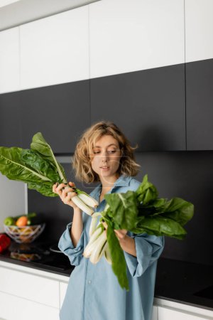 durchbohrte junge Frau betrachtet frische und grüne Kohlblätter in der Küche 