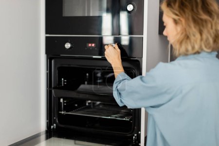 young woman with wavy hair using modern oven in kitchen 