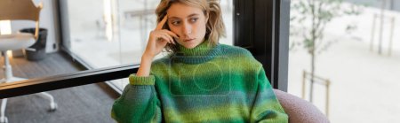 thoughtful young woman in green sweater sitting in lobby of hotel in Barcelona, banner 
